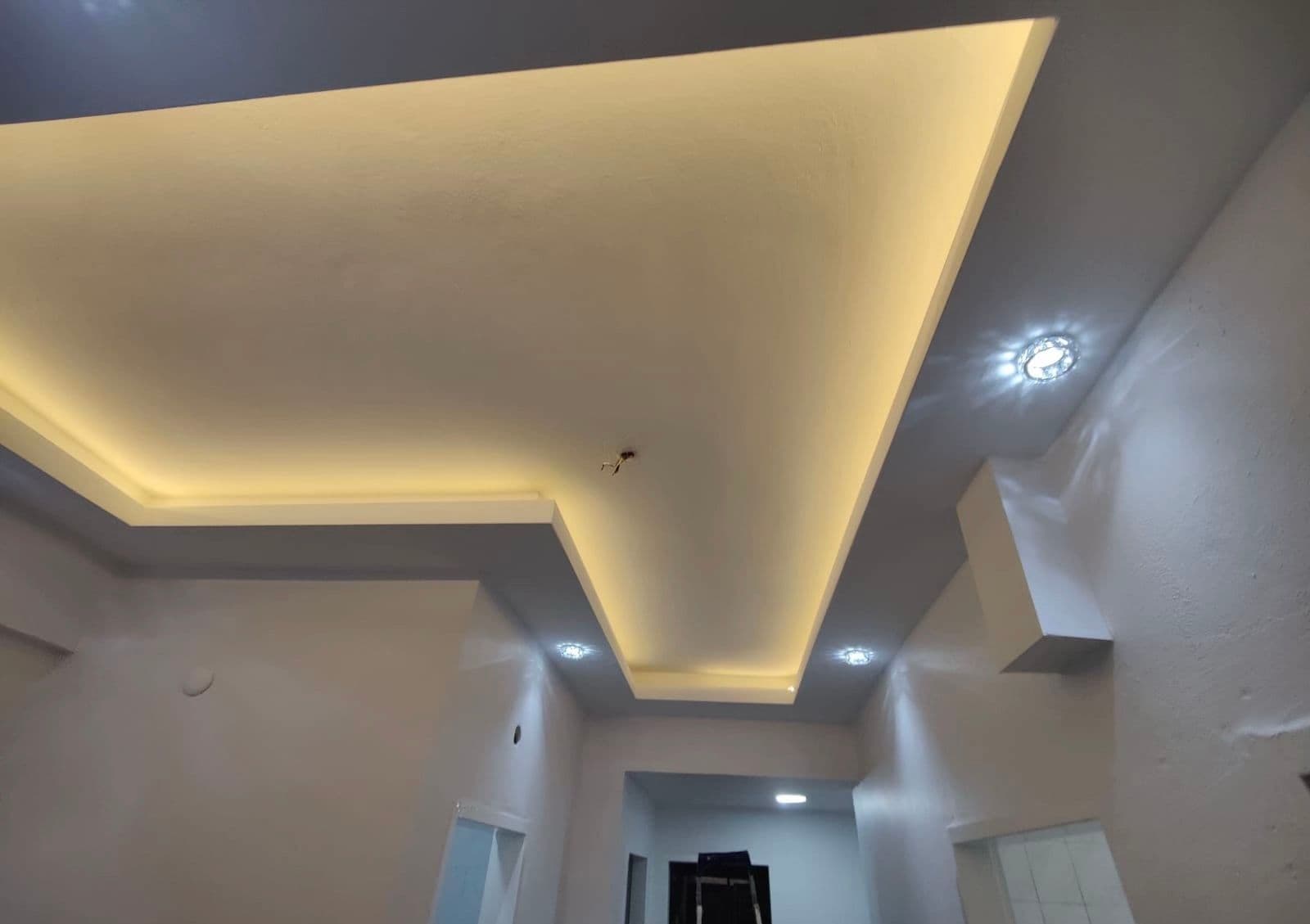 Bitmiş kademeli alçıpan tavan; gizli LED aydınlatmalı koridor, spot aydınlatmalar, arkada iskele görünür.